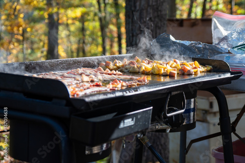 Bacon and potatoes cooking on an outdoor griddle photo