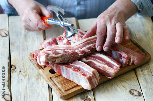 The chef cuts raw pork ribs on a wooden board. Selective focus. Cooking the ribs.