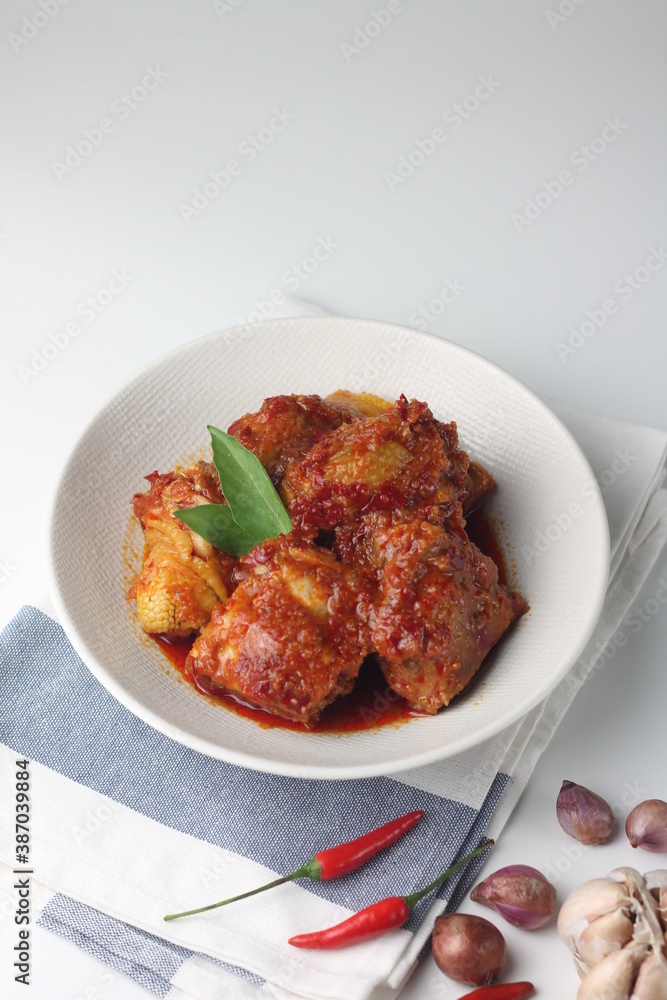 Ayam Bumbu Bali or Ayam bumbu Balado or Ayam Masak merah, Indonesian traditional chicken spicy, served on ceramic plate. Usually eat with yellow rice or nasi lemak. Isolated background. Copy space. Ayam Bumbu Bali or Ayam bumbu Balado or Ayam Masak merah, Indonesian traditional chicken spicy, served on ceramic plate. Usually eat with yellow rice or nasi lemak. Isolated background. Copy space.