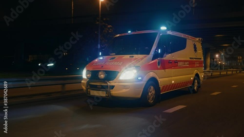 Parallel Moving Footage of an Ambulance Vehicle with Working Strobe Light and Signal Driving to Emergency Call on a City Urban Street at Night photo