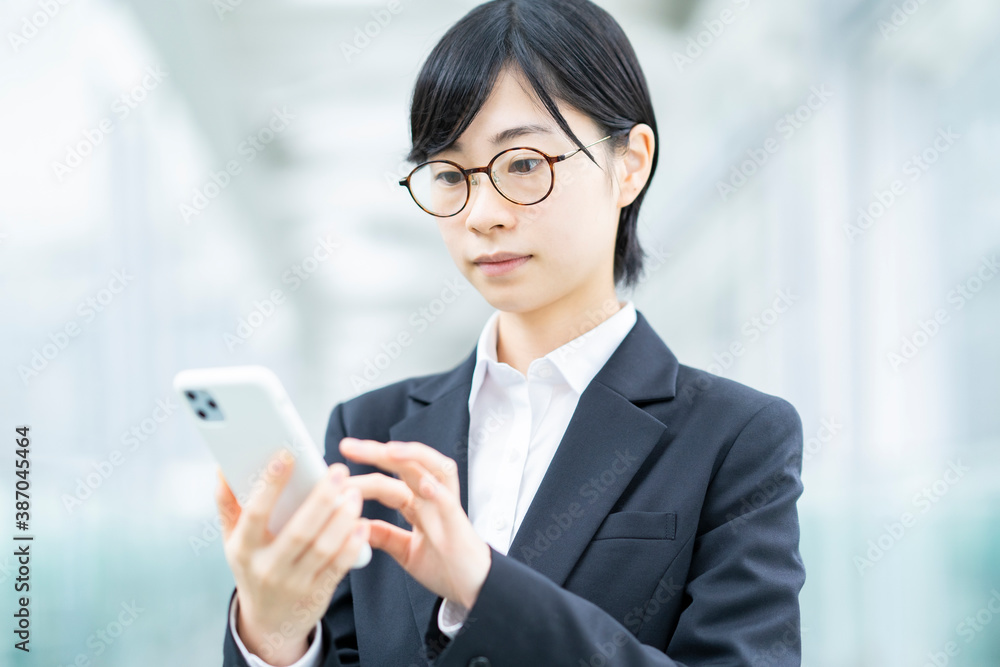 スマートフォンを操作するスーツ姿の若い女性 スマートフォンを操作するスーツ姿の若い女性