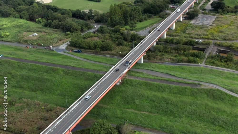 Vehicles Driving And Travelling Across the Overpass Bridge Over The Lush Green Fields Overlooking The Golf Course And Fujimi City In Saitama, Japan. - aerial, tilt-up shot Vehicles Driving And Travelling Across the Overpass Bridge Over The Lush Green Fields Overlooking The Golf Course And Fujimi City In Saitama, Japan. - aerial, tilt-up shot