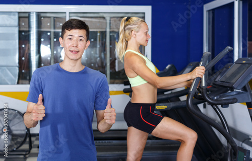Young sporty man coach posing in gym with fitness machines on background