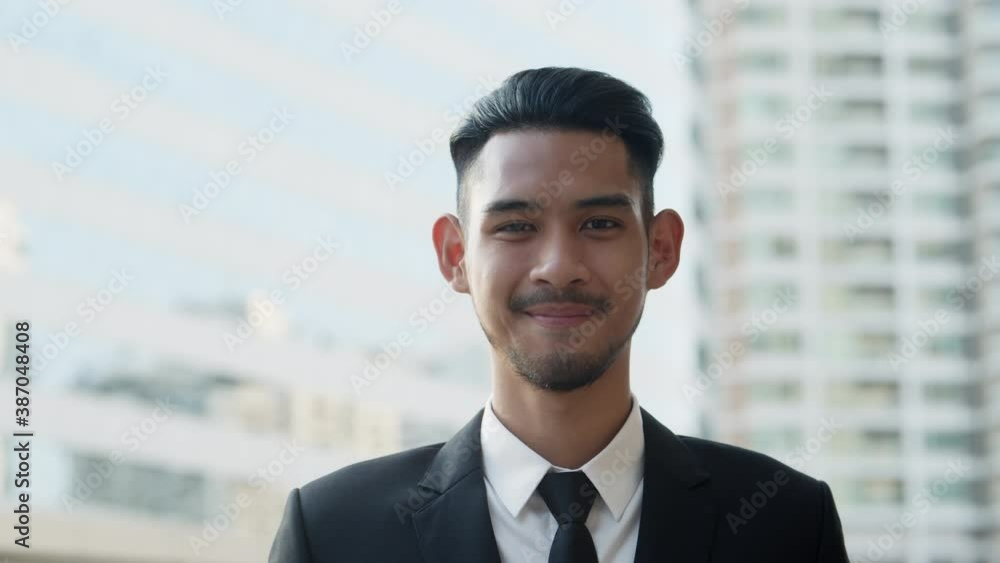 Medium close up. Portrait of Handsome young businessman standing outside the office and smiling happily On the background of city building Medium close up. Portrait of Handsome young businessman standing outside the office and smiling happily On the background of city building