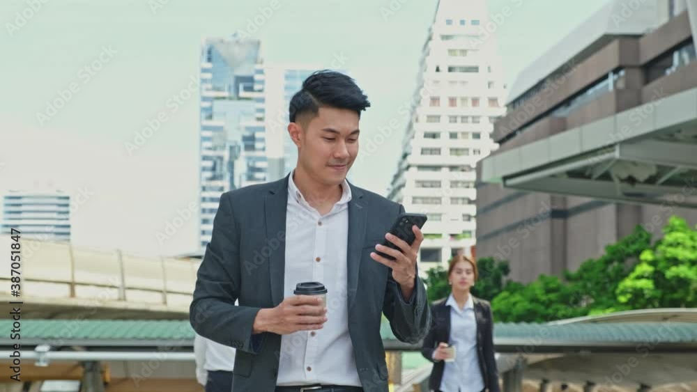 Asian young businessman using smartphone while walking to the office. Asian young businessman using smartphone while walking to the office.