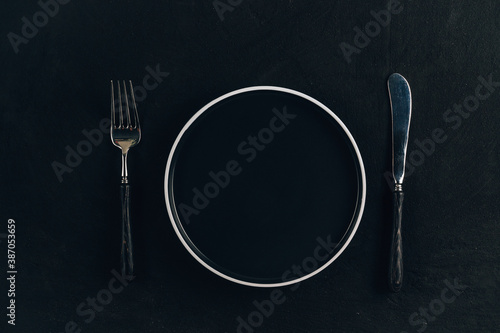Elegant black table setting: plate and silverware over black background.