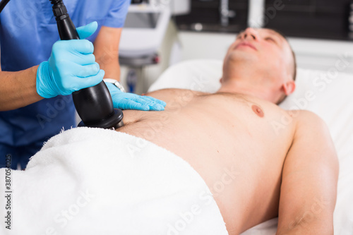 Woman doctor is doing vacuum massage procedure on belly of adult client in clinic.