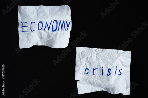 Inscription "Economy crisis" on two crumpled paper sheets against black background. Global world economy collapse concept. Top view