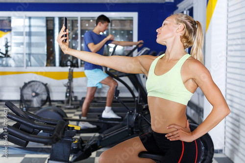 young female athlete taking selfie during training in fitness center