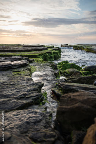 Rocks covered with green moss on the coastline with lapping waves at sunrise © LightItUp