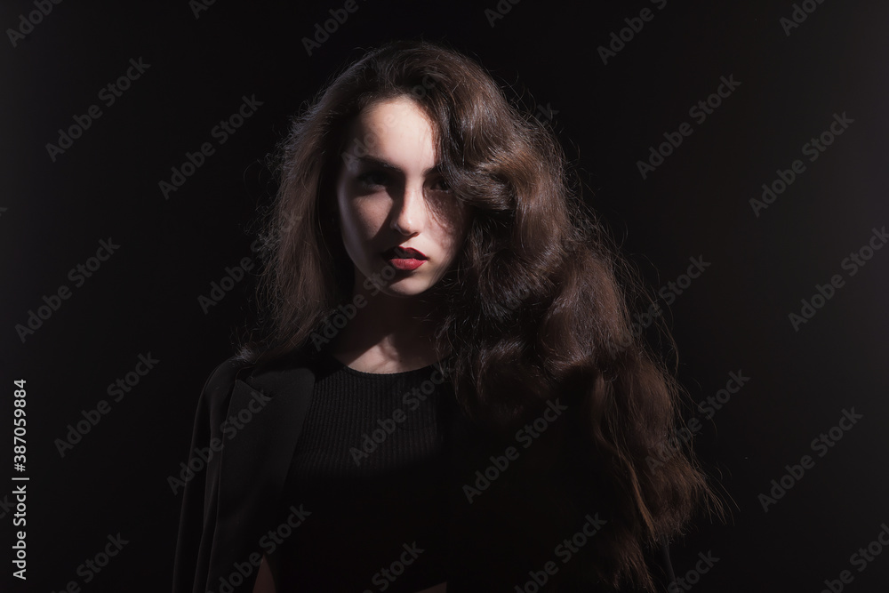 Vintage portrait with harsh light of a beautiful, slim brunette woman with bright makeup and wavy hair