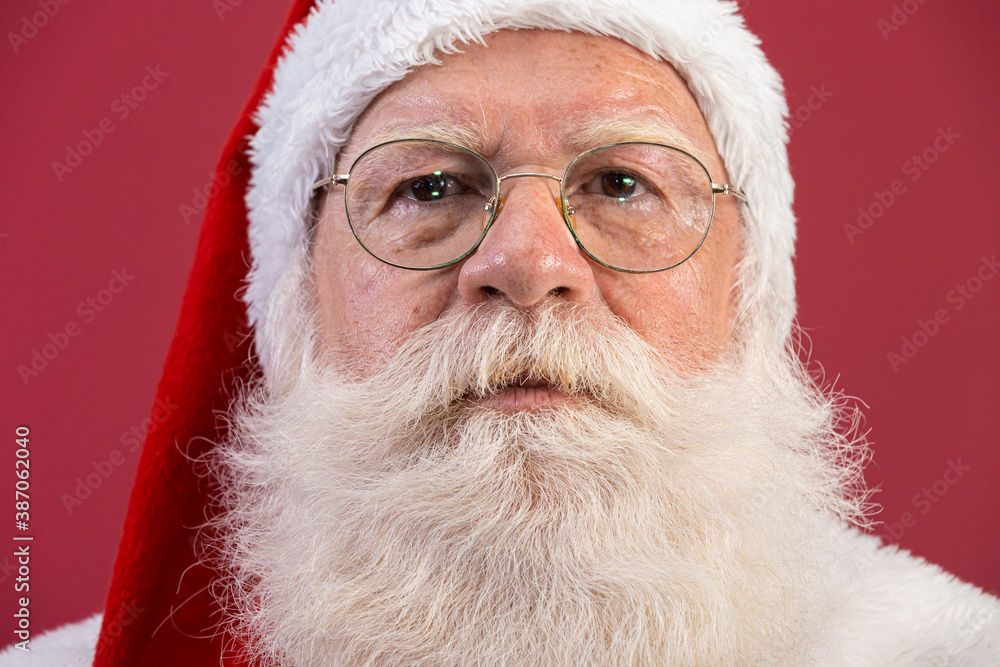 Real Santa Claus with a red background, wearing glasses, gloves and a hat looking camera. Close-up. Real Santa Claus with a red background, wearing glasses, gloves and a hat looking camera. Close-up.