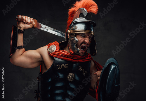 Photo Attacking savage and brutal imperial soldier from rome in steel armour and red cloak holding sword and shield in dark background
