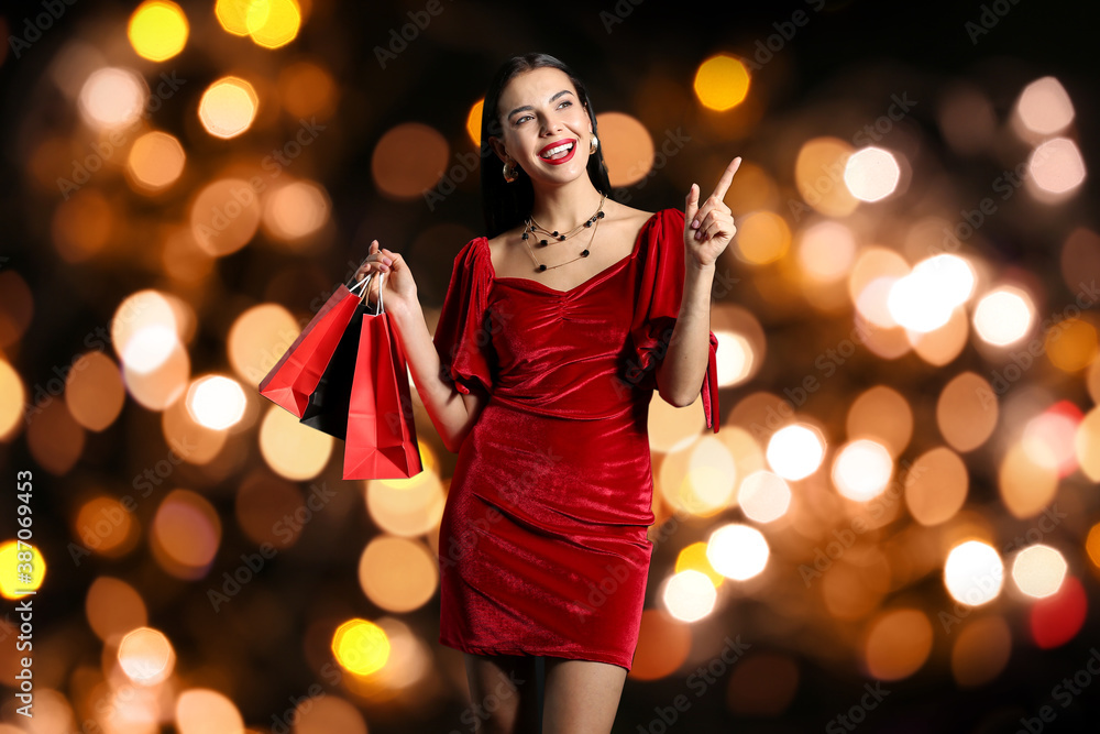 Beautiful young woman with shopping bags against blurred golden lights on dark background. Black Friday sale Beautiful young woman with shopping bags against blurred golden lights on dark background. Black Friday sale
