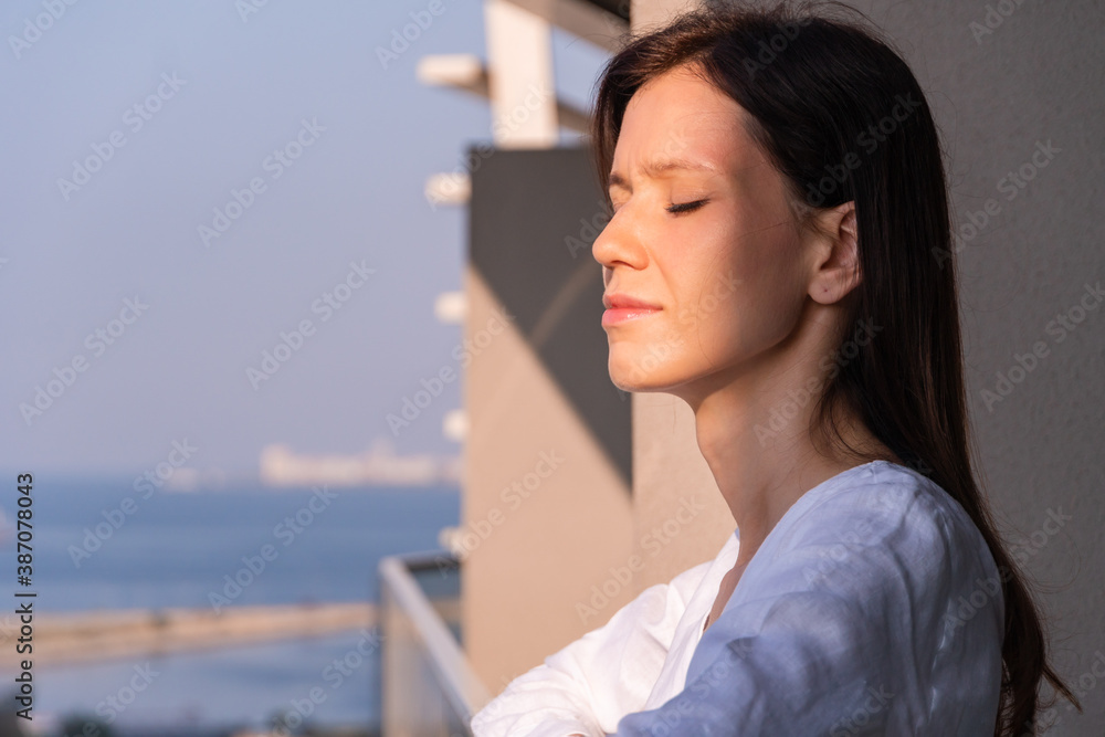 Young woman stays on balcony and enjoy of sunny morning