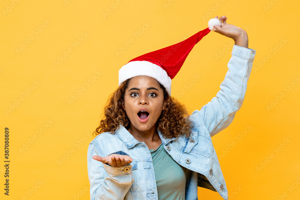 Funny surprised African American woman wearing Christmas hat with open palm gesture on yellow isolated background Funny surprised African American woman wearing Christmas hat with open palm gesture on yellow isolated background