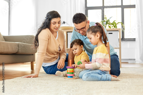 family and people concept - happy mother, father, little daughter and baby son playing with pyramid toy at home