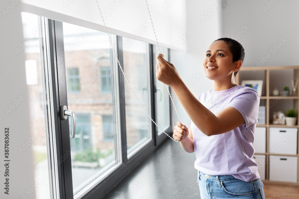 people and leisure concept - happy young african american woman opening window roller blinds at home people and leisure concept - happy young african american woman opening window roller blinds at home