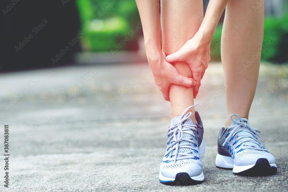 Runner female touching painful twisted or broken ankle. Athlete training accident. Sport sprain cause injury knee leg bones while run in outdoor the park. 