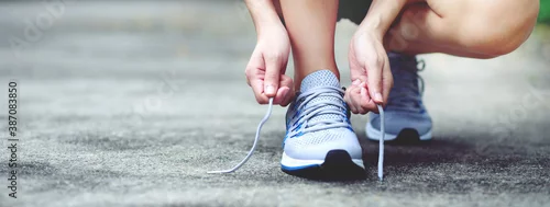 Obraz Running shoes. close up female athlete tying laces for jogging on road. Runner ties getting ready for training. Sport lifestyle. copy space banner.