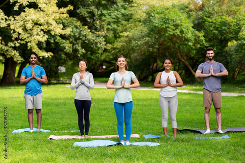 fitness, sport and healthy lifestyle concept - group of happy people doing yoga at summer park