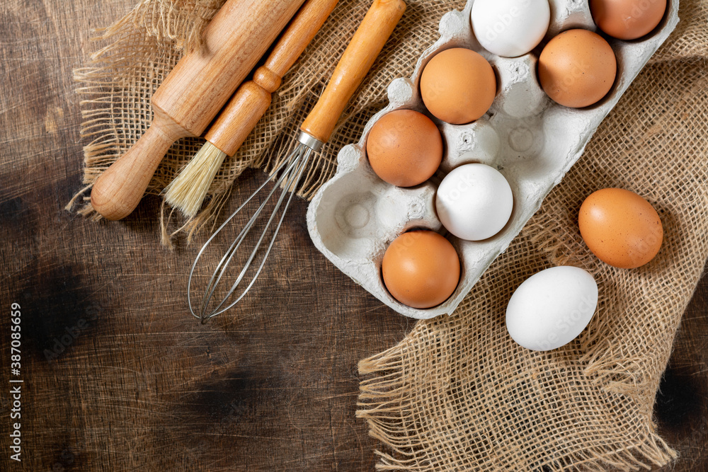 Eggs in a tray on the kitchen table. White and brown eggs with a whisk and rolling pin. Chicken eggs and whisk on a culinary background. Concept of preparation for baking. Top view with copyspace Eggs in a tray on the kitchen table. White and brown eggs with a whisk and rolling pin. Chicken eggs and whisk on a culinary background. Concept of preparation for baking. Top view with copyspace