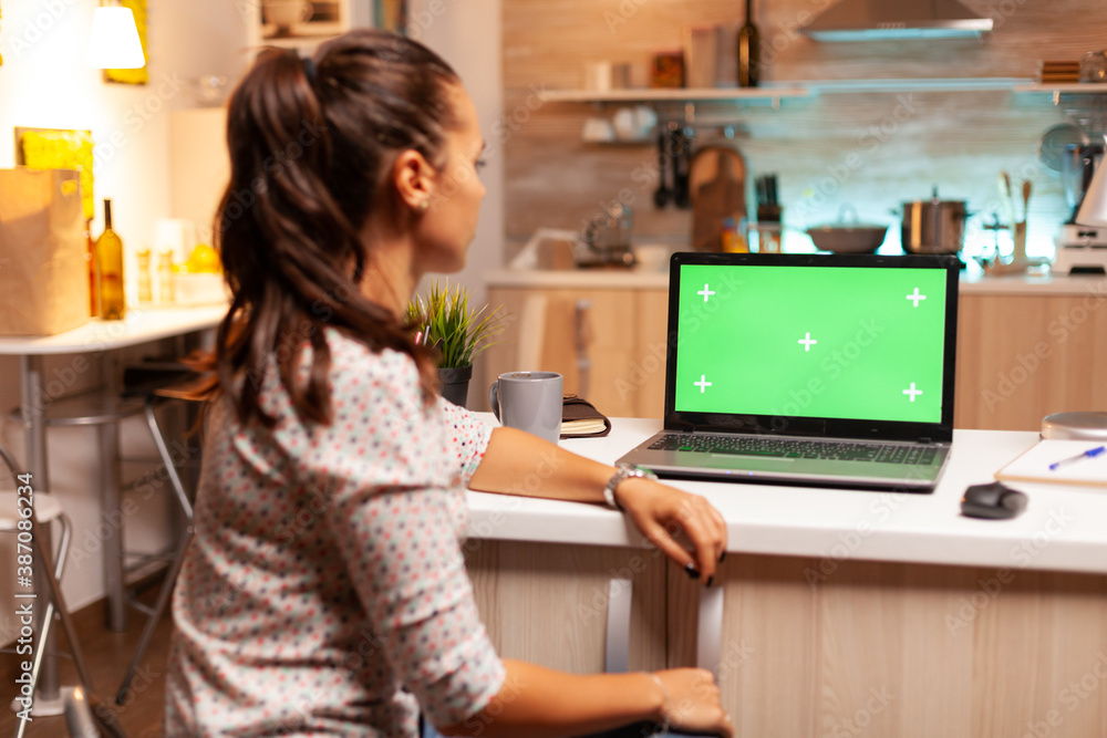 Woman looking at laptop with green mockup during night time in home kitchen. Sitting at desk works on computer late at night, business, online, smart, blank, copyspace. Woman looking at laptop with green mockup during night time in home kitchen. Sitting at desk works on computer late at night, business, online, smart, blank, copyspace.