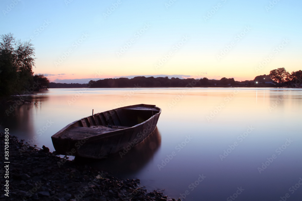 Naklejka premium Una vieja barca de remos amarrada al atardecer en el delta del Danubio, Rumanía. Atardecer en la desembocadura del río Danubio en el pueblo de Nufaru.