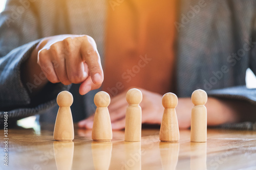 Businesswoman choosing and pointing finger at wooden people from a group of employees while working in the office