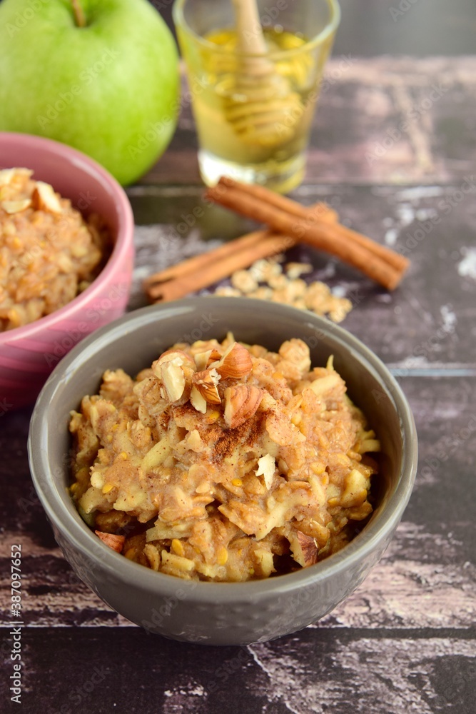 Hot breakfast oat porridge with apple, hazelnuts, honey and cinnamon powder on a wooden rustic background. Hot breakfast oat porridge with apple, hazelnuts, honey and cinnamon powder on a wooden rustic background.