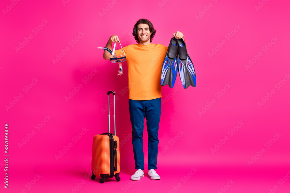 Full length photo of man baggage hold mask flips wear orange t-shirt jeans sneakers isolated pink color background Full length photo of man baggage hold mask flips wear orange t-shirt jeans sneakers isolated pink color background
