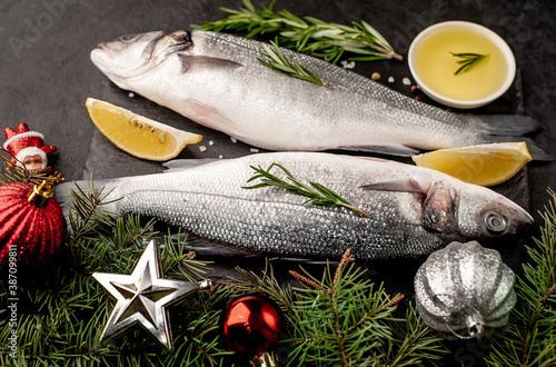 Raw sea bass fish with spices for the Christmas holiday on a stone background with a Christmas tree and new year toys