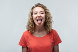 Portrait of cute blonde girl sticking out her tongue at camera. Human emotions concept. Studio shot, white background