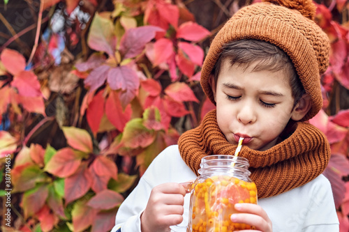 cute fashionable boy holding a sea buckthorn drink on a background of wild grapes.