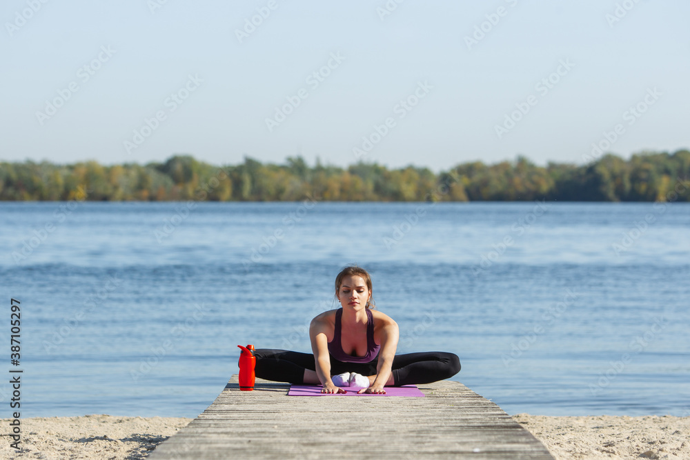 Stretching. Young female athlete, woman training, practicing outdoors in autumn sunshine. Beautiful caucasian sportswoman doing yoga open-air. Concept of sport, healthy lifestyle, movement, activity.