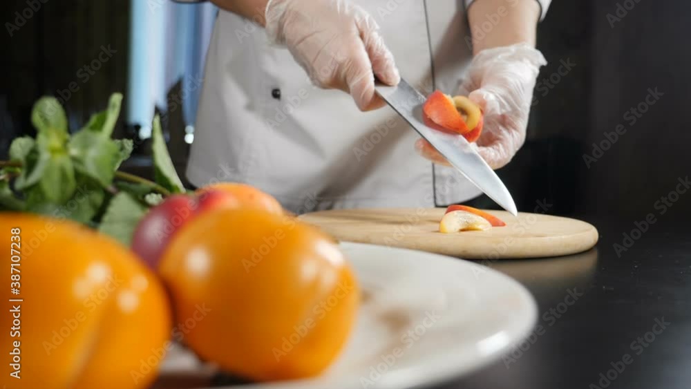 Female chef slicing peach with kitchen knife in slow motion on background. Shot with fresh fruit in foreground. Food video. Cooking organic salad. Full hd Female chef slicing peach with kitchen knife in slow motion on background. Shot with fresh fruit in foreground. Food video. Cooking organic salad. Full hd