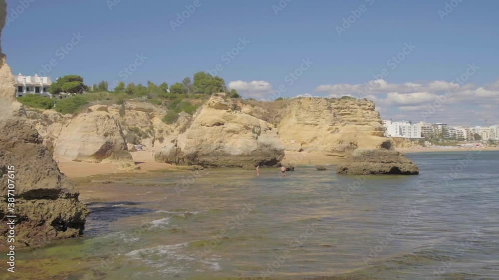 Drone flies low around Sea Cliff with luxury white hotel with palm trees perched up on top and people in water Drone flies low around Sea Cliff with luxury white hotel with palm trees perched up on top and people in water