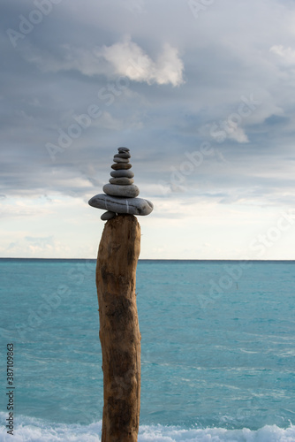 cairn fait de galets posé en équilibre sur un poteau en bois suspendu entre ciel et mer © Christophe