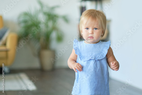 Portrait of a pretty little baby girl in a blue dress. cute blonde babe in the living room