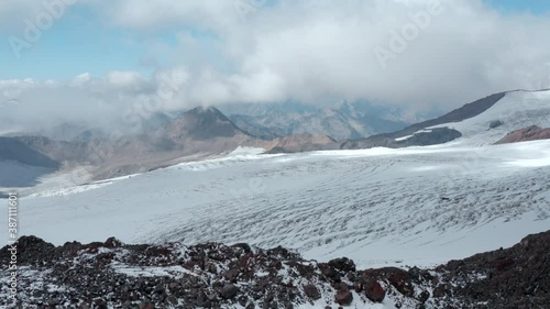 Red shelter station for skiers and tourists on snowy glacier ice cracks slope of Elbrus mountain under sky with clouds on sunny day aerial view. photo