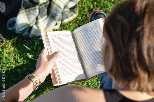 Shot from above of a woman reading a book sitting on a green lawn