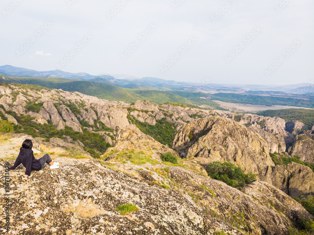 Female traveller sits on the rock and enjoys panoramic view of Birtvisi canyon rock formations. Georgia travel and hiking.