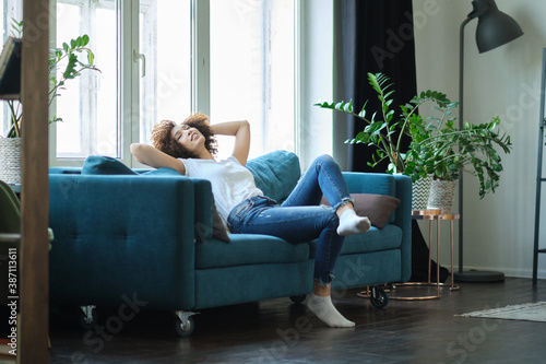 Attractive young woman relaxing on a sofa at home hands behind her head © yavdat