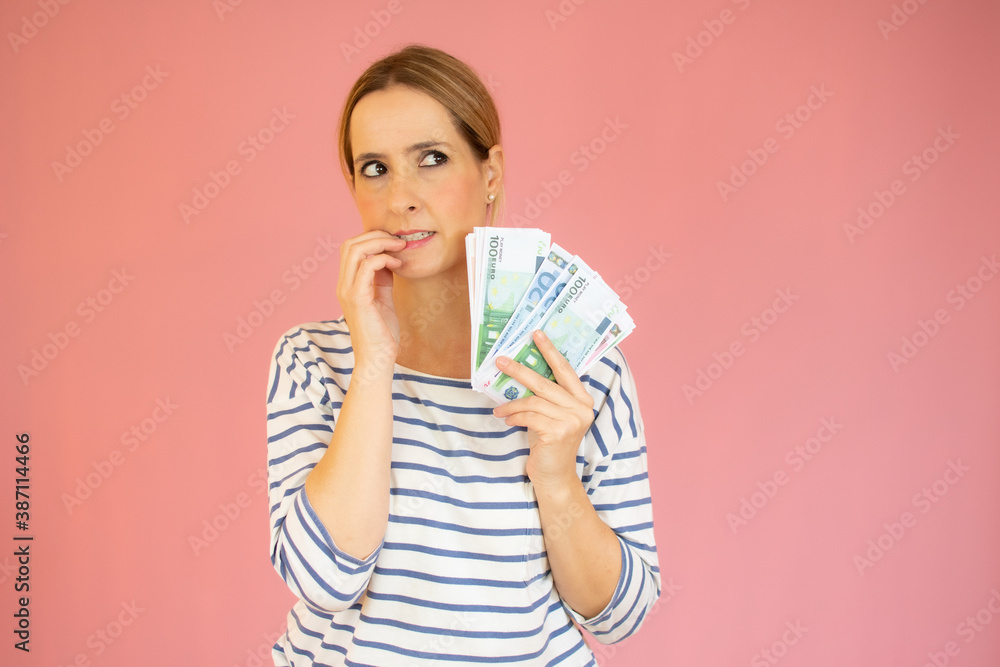 Beautiful young woman holding money looking stressed and nervous with hands on mouth biting nails. anxiety problem. Beautiful young woman holding money looking stressed and nervous with hands on mouth biting nails. anxiety problem.