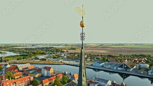 Tall spire on a large medieval church made from red bricks. Spire features a golden weathercock and panoramic view over an old European town. 4K aerial video. photo