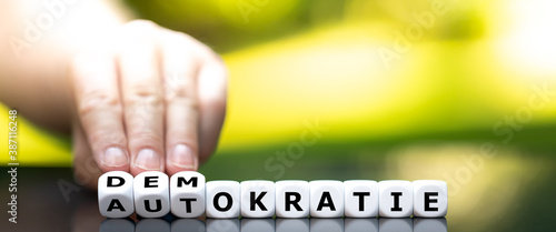 Foto Hand turns dice and changes the German word Autokratie (autocracy) to Demokratie (democracy)
