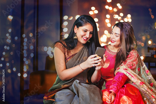 Two beautiful Indian women in ethnic clothes doing Diwali shopping online, using app on mobile phone