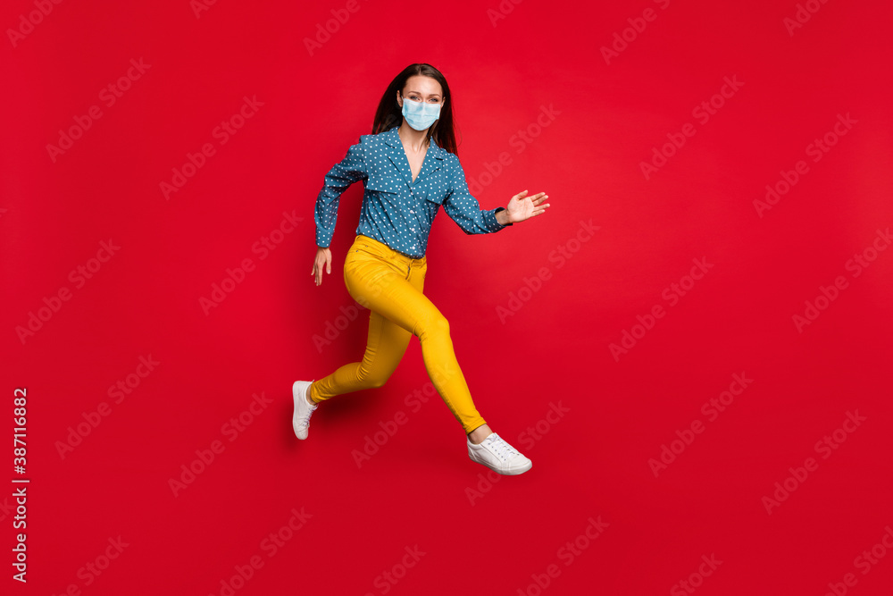Full length view of attractive fit cheerful girl jumping running active motion wear mask isolated bright red color background