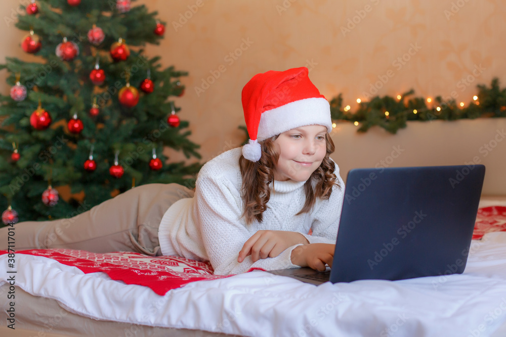 Christmas greetings online. A smiling girl uses a laptop book to make video calls to friends and parents. Christmas greetings online. A smiling girl uses a laptop book to make video calls to friends and parents.