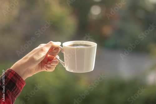 A female hand holds a white cup with coffee